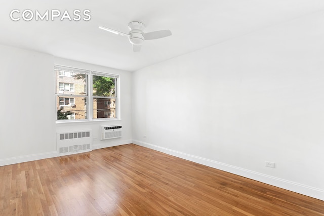 unfurnished room with radiator, a wall mounted air conditioner, baseboards, and wood finished floors