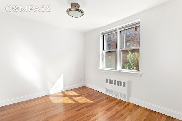 empty room featuring light wood-type flooring, baseboards, and radiator