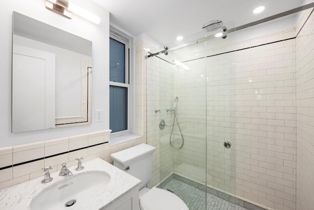 bathroom with vanity, toilet, a shower with shower door, and tile walls