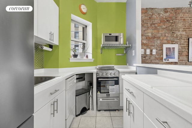 kitchen featuring light tile patterned floors, sink, appliances with stainless steel finishes, white cabinetry, and brick wall