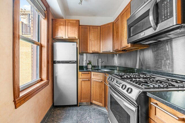 kitchen with stainless steel appliances, sink, dark stone countertops, and backsplash