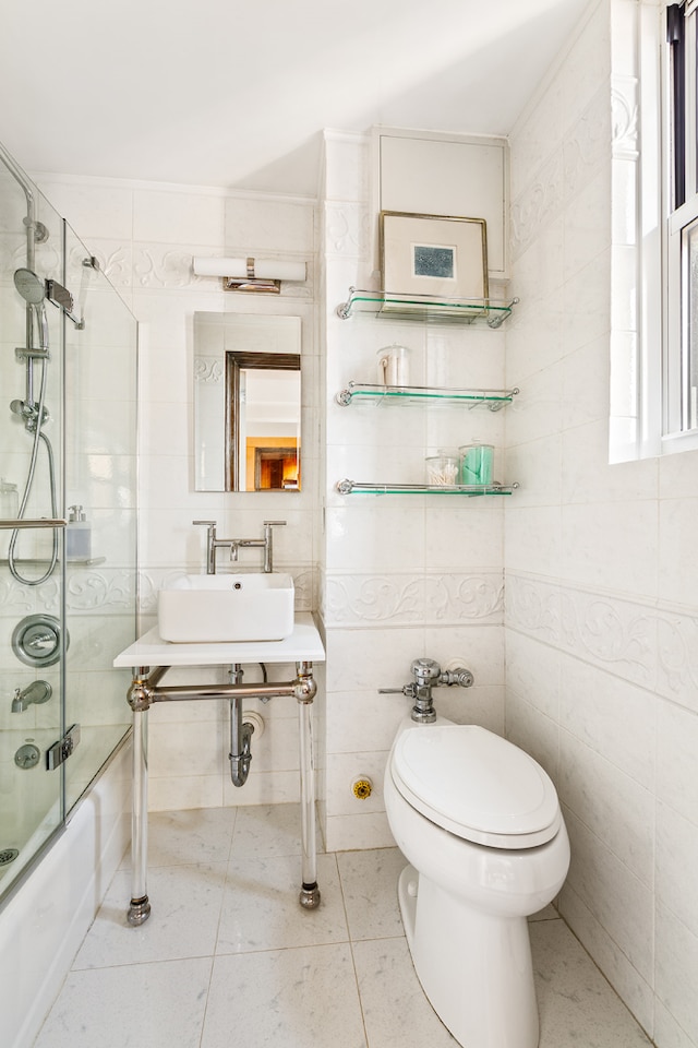 bathroom with toilet, a sink, tile walls, combined bath / shower with glass door, and tile patterned floors