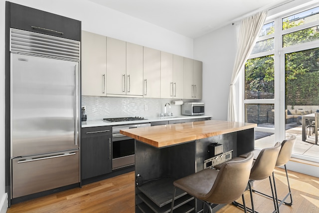 kitchen with light wood-style flooring, stainless steel appliances, a sink, wooden counters, and a kitchen bar