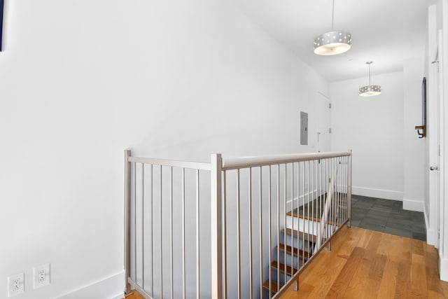 hallway with electric panel, baseboards, wood finished floors, and an upstairs landing