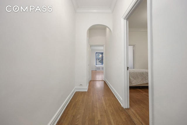 hall featuring arched walkways, wood finished floors, baseboards, and ornamental molding