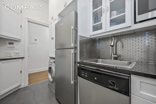 kitchen with dark countertops, washer / dryer, white cabinets, stainless steel appliances, and a sink