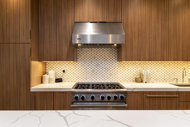 kitchen featuring brown cabinetry, wall chimney exhaust hood, modern cabinets, hanging light fixtures, and high end stainless steel range oven