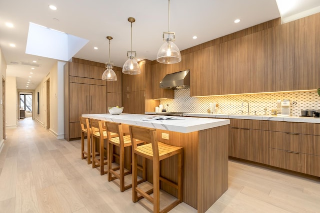 kitchen with wall chimney range hood, backsplash, a large island, and modern cabinets