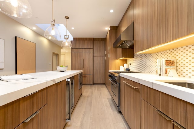kitchen with brown cabinets, wall chimney range hood, high end appliances, and light wood finished floors