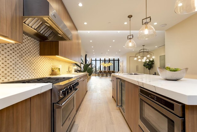 kitchen with decorative backsplash, appliances with stainless steel finishes, hanging light fixtures, light wood-style floors, and exhaust hood