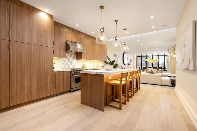 kitchen with stainless steel stove, under cabinet range hood, open floor plan, light countertops, and modern cabinets