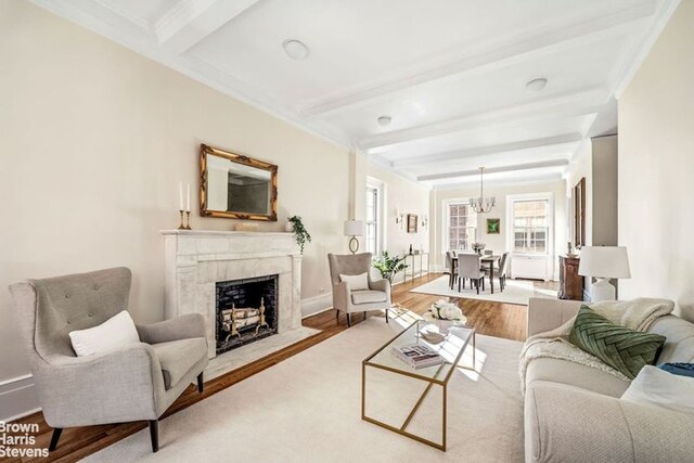 living room featuring beam ceiling, a notable chandelier, wood-type flooring, ornamental molding, and a high end fireplace