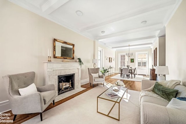 living room featuring hardwood / wood-style floors, beam ceiling, ornamental molding, a premium fireplace, and an inviting chandelier