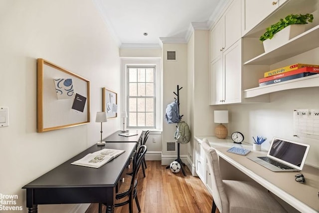 home office with baseboards, visible vents, light wood-style flooring, ornamental molding, and built in desk