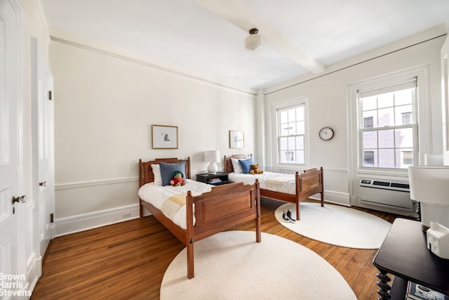 bedroom with beam ceiling, wood finished floors, baseboards, and a wall mounted AC