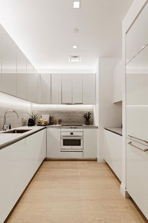 kitchen featuring light hardwood / wood-style flooring, white cabinetry, backsplash, sink, and oven