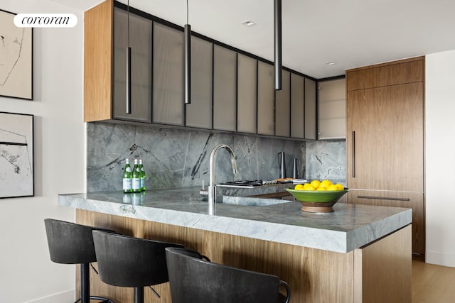 kitchen with tasteful backsplash, a breakfast bar area, light wood-type flooring, and kitchen peninsula