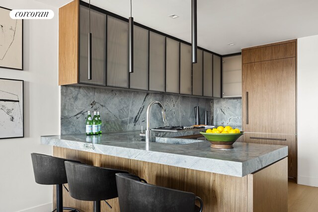 kitchen with backsplash, a peninsula, wood finished floors, and a breakfast bar area