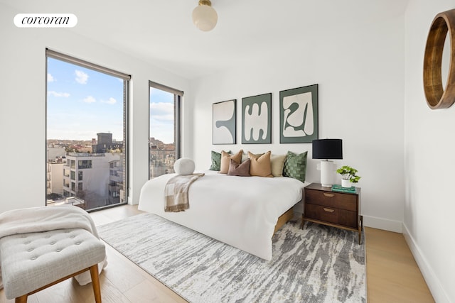 bedroom featuring light wood-type flooring, visible vents, baseboards, and a view of city