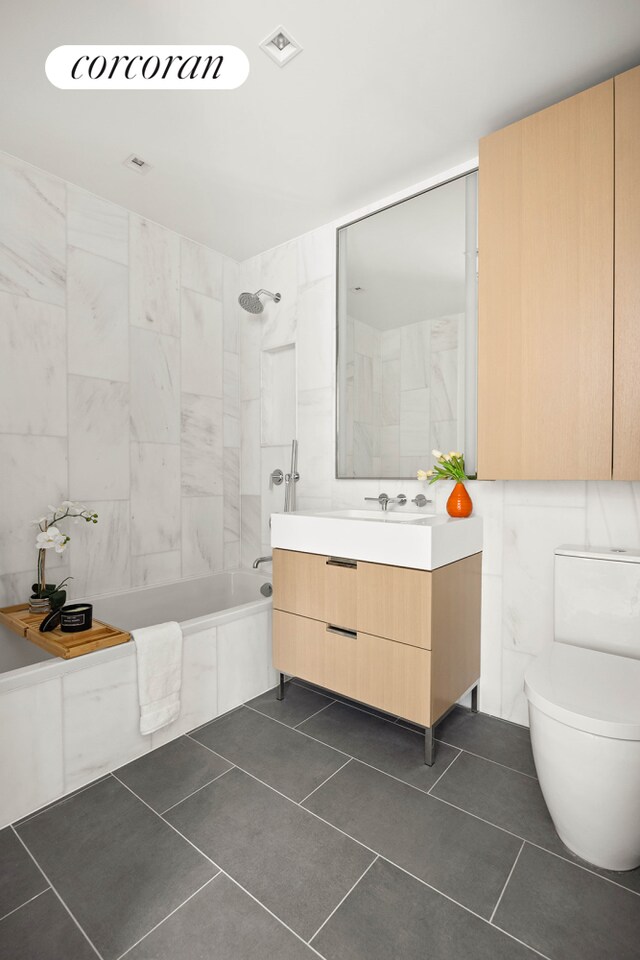 full bathroom with tile walls, tile patterned flooring, vanity, tiled shower / bath combo, and toilet