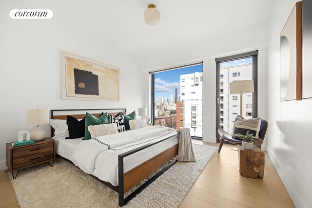 bedroom with visible vents, baseboards, a view of city, light wood-style floors, and access to outside