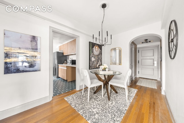 dining area featuring arched walkways, an inviting chandelier, baseboards, and wood finished floors