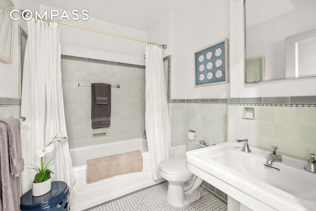 bathroom with a wainscoted wall, toilet, shower / bath combo, tile walls, and a sink