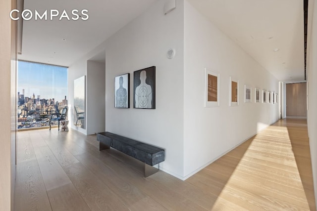 hallway with expansive windows, a view of city, and wood finished floors