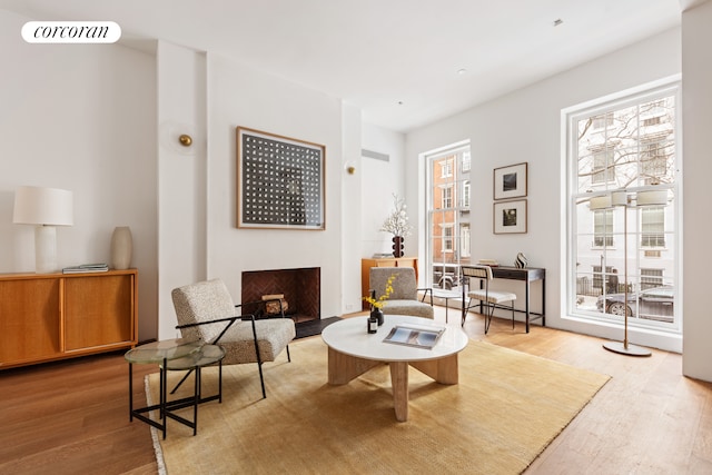 living area with a fireplace with flush hearth, wood finished floors, and visible vents