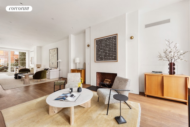 living area featuring light wood-type flooring, visible vents, and a fireplace