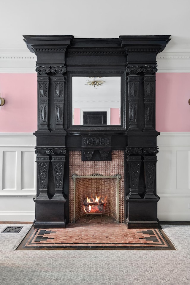 details featuring crown molding, a lit fireplace, wainscoting, and a decorative wall
