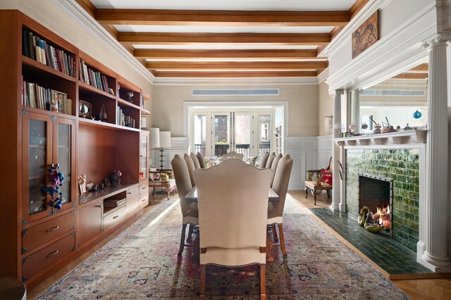 dining space with a fireplace, ornamental molding, beam ceiling, and a decorative wall