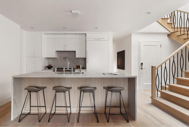 kitchen with tasteful backsplash, white cabinetry, a kitchen bar, a kitchen island with sink, and light hardwood / wood-style floors