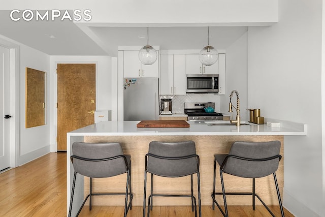 kitchen with sink, backsplash, white cabinets, stainless steel appliances, and light wood-type flooring