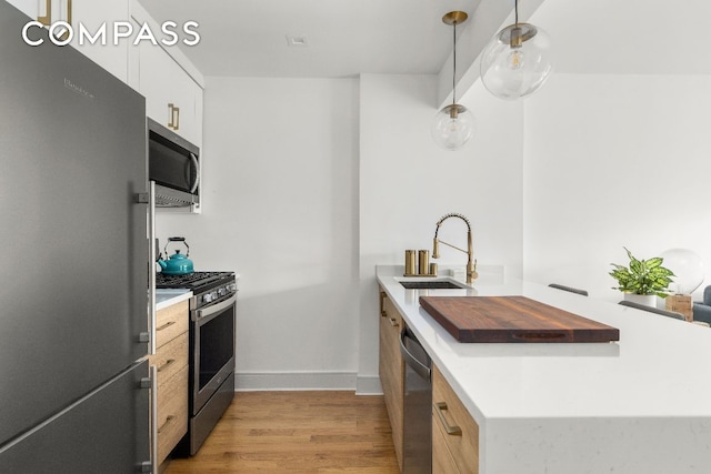 kitchen with appliances with stainless steel finishes, sink, white cabinetry, light hardwood / wood-style floors, and hanging light fixtures