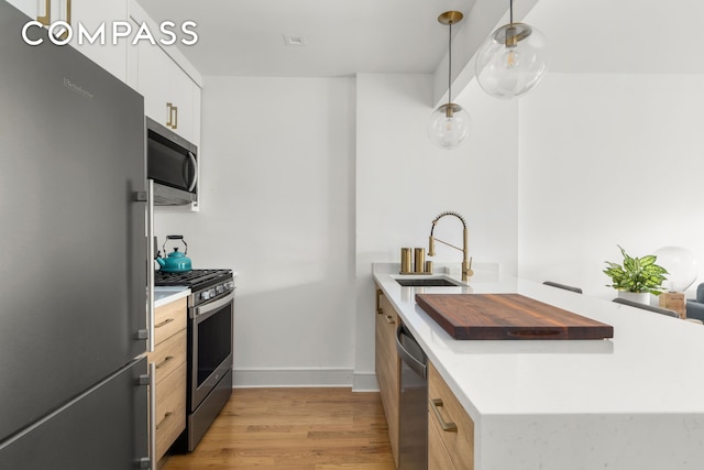 kitchen with light wood finished floors, stainless steel appliances, white cabinets, a sink, and a peninsula