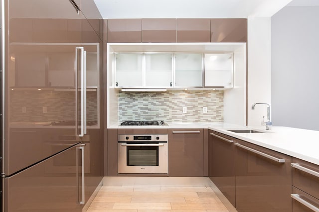 kitchen featuring tasteful backsplash, wall oven, light countertops, stainless steel gas stovetop, and a sink