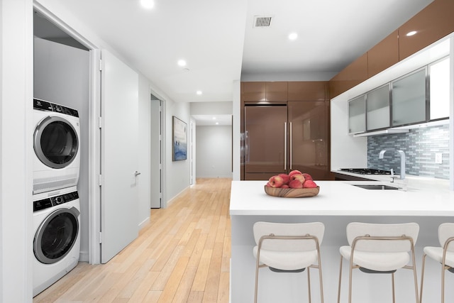 kitchen with light wood-type flooring, built in refrigerator, stacked washer and clothes dryer, a sink, and tasteful backsplash