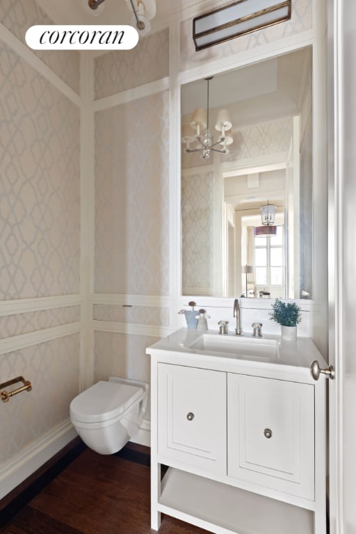 half bath featuring wallpapered walls, baseboards, wood finished floors, and vanity