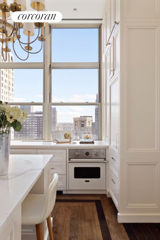 kitchen with dark wood-type flooring, white cabinetry, a notable chandelier, light stone countertops, and oven