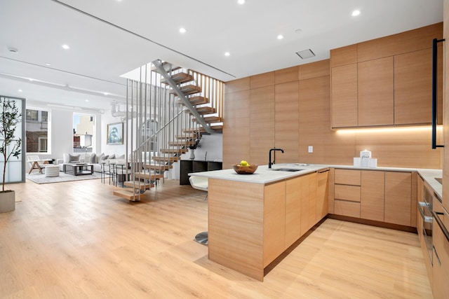 kitchen featuring light brown cabinets, light wood-style flooring, a peninsula, a sink, and modern cabinets