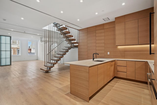 kitchen featuring a peninsula, a sink, open floor plan, light wood-type flooring, and modern cabinets