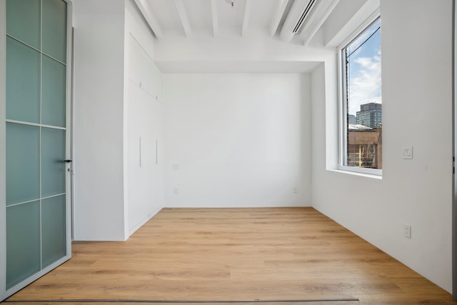 empty room featuring light wood finished floors and beamed ceiling