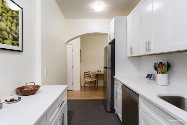 kitchen with tasteful backsplash, arched walkways, dishwasher, light countertops, and white cabinetry