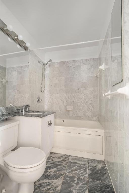 full bathroom with vanity, toilet, tiled shower / bath combo, and tile walls