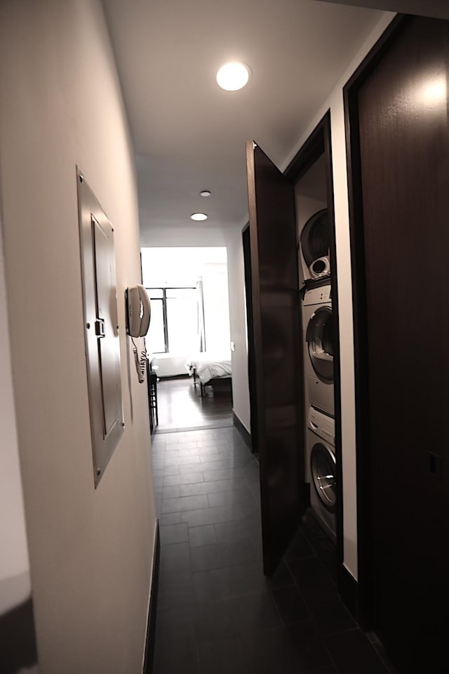 hallway featuring stacked washing machine and dryer, dark tile patterned floors, recessed lighting, and baseboards