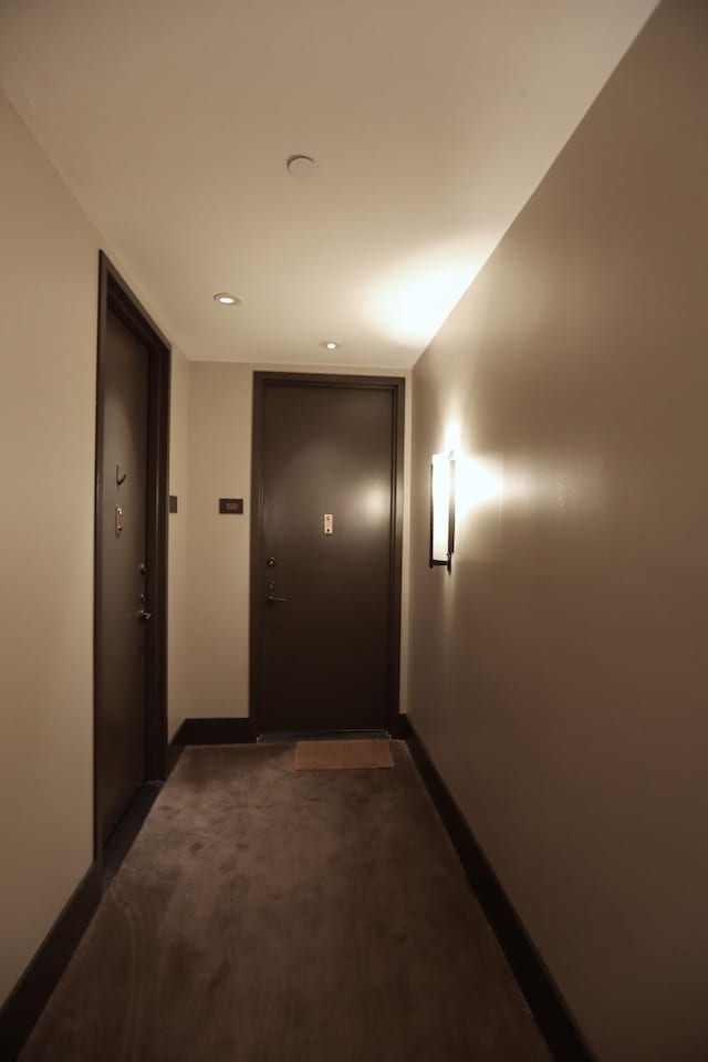 hall featuring baseboards and dark carpet