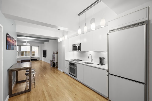 kitchen featuring appliances with stainless steel finishes, sink, white cabinets, and decorative light fixtures