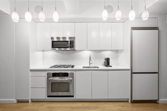 kitchen featuring sink, light hardwood / wood-style flooring, white cabinetry, stainless steel appliances, and decorative light fixtures