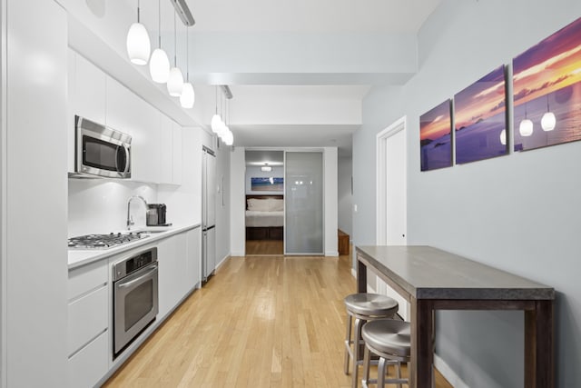 kitchen with appliances with stainless steel finishes, white cabinetry, sink, hanging light fixtures, and light hardwood / wood-style floors